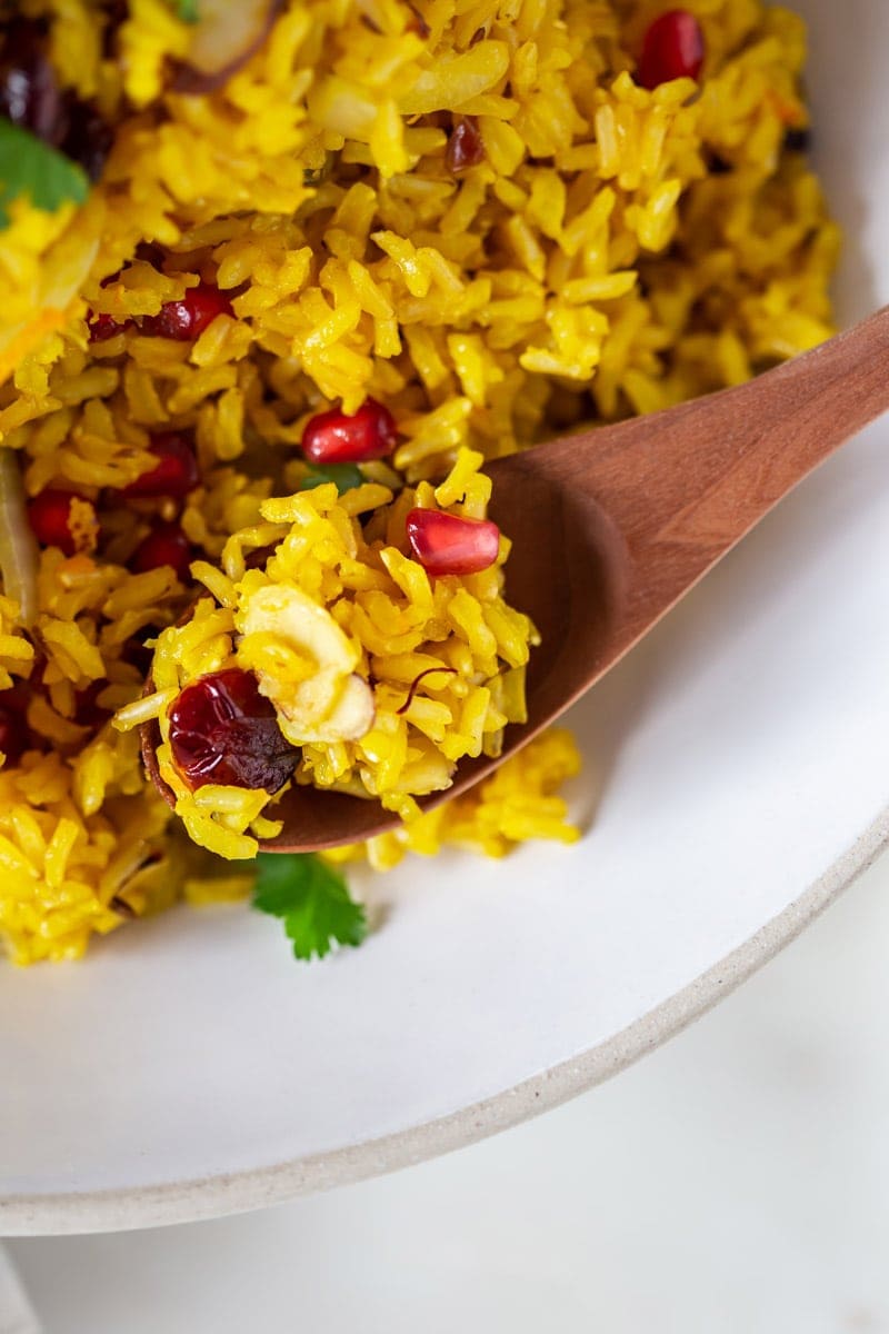 Close up of a wooden spoon filled with saffron rice, with visible saffron threads