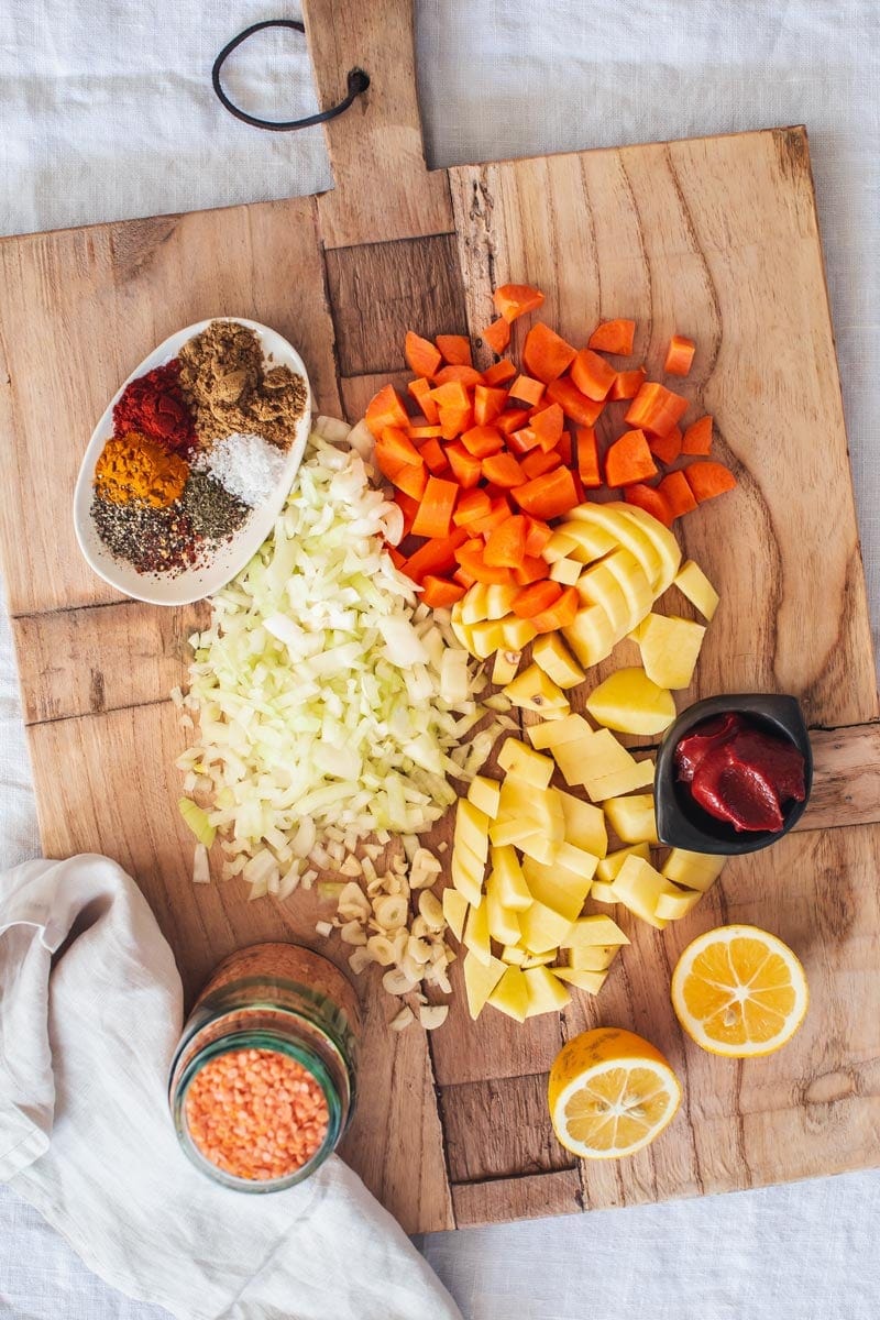 A wooden board with all the ingredients for making lentil soup laid out over it