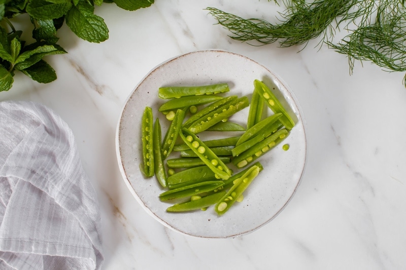 Sugar snaps with their ends trimmed, sliced in half lengthways revealing the peas inside