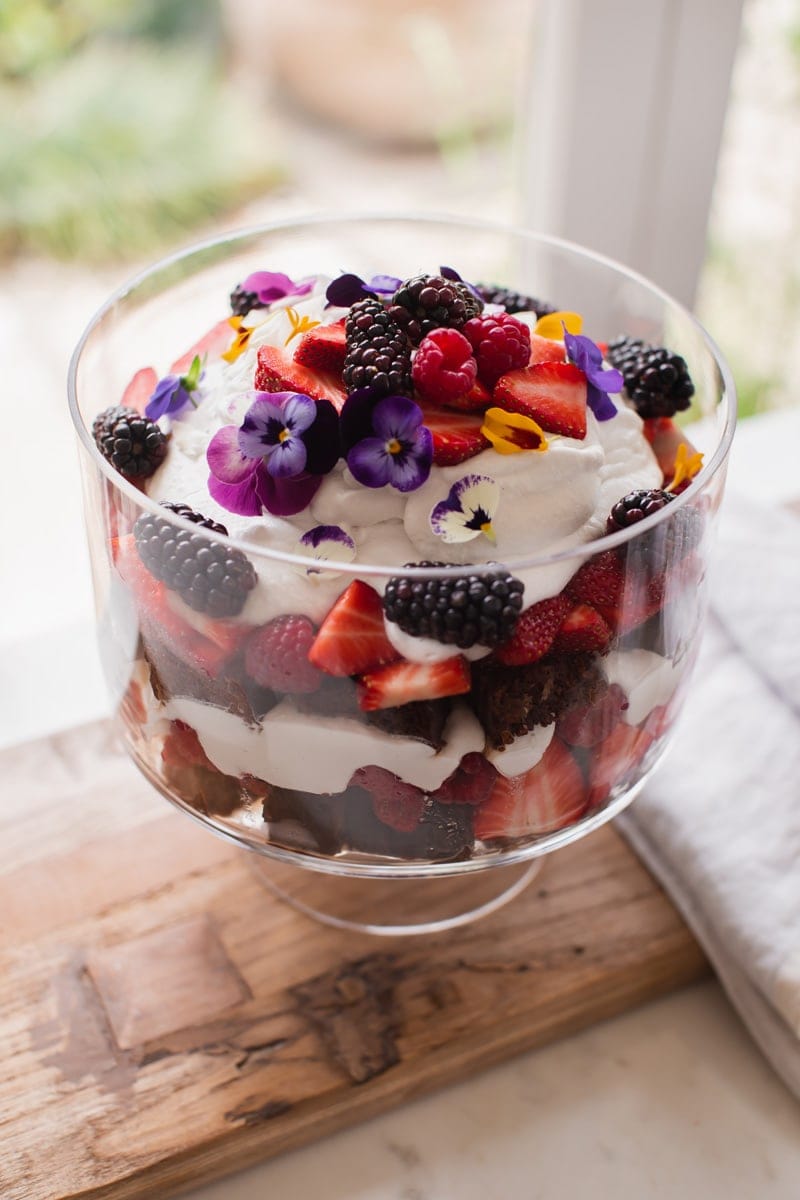 Summer berry trifle decorated with flower petals, standing by the kitchen window