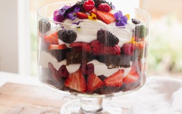 Side profile of berry trifle with fruit and flower petals on top.
