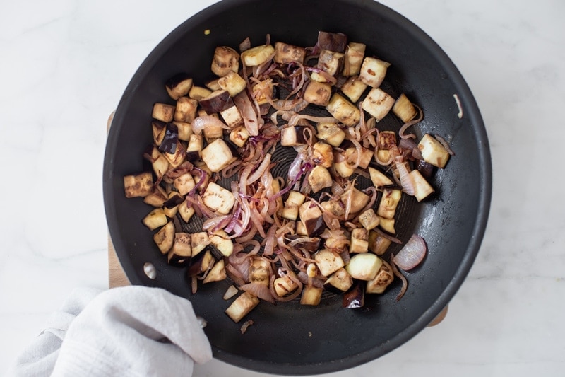 Cubed eggplant and red onion in a frying pan