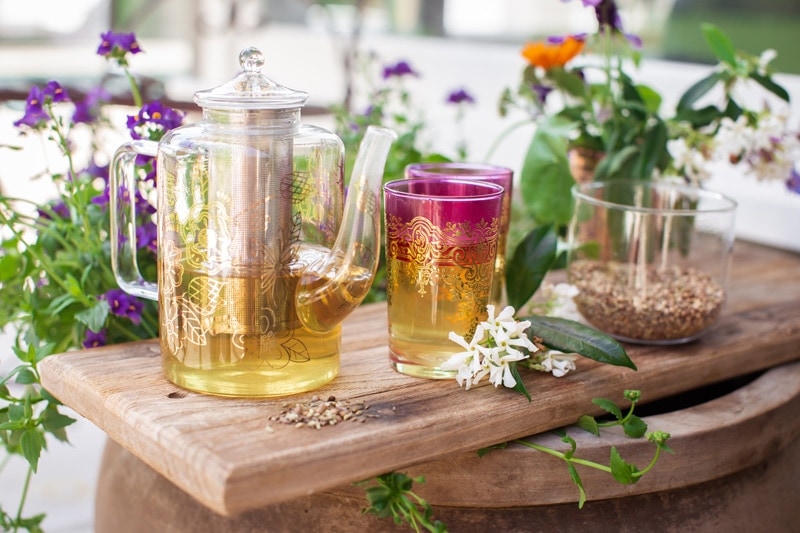 Teapot and glass filled with hot tea on a bench in the garden