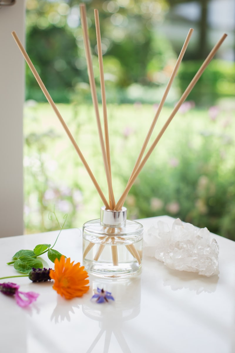 Reed diffuser in the foreground, lush garden landscape in the background.