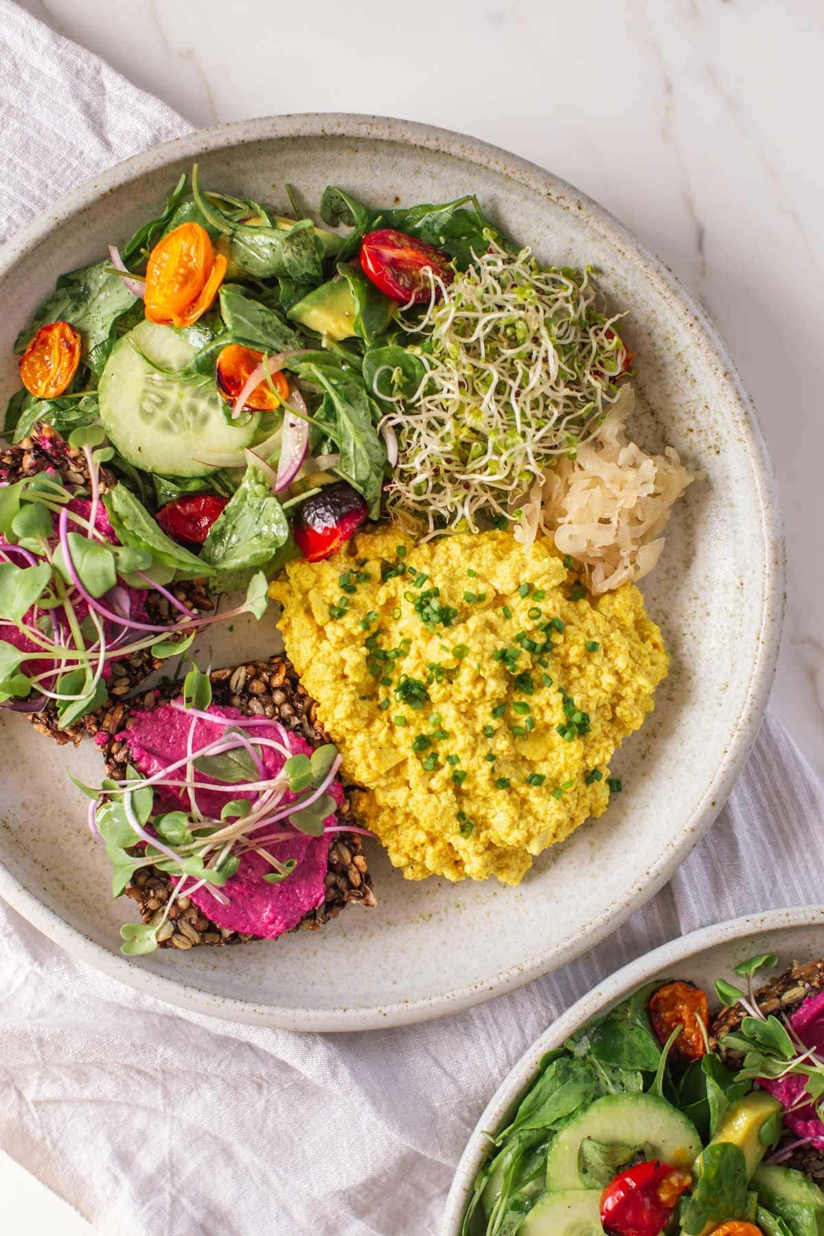 Plate filled with a healthy vegan breakfast of scrambled tofu with salad, sprouts and kraut