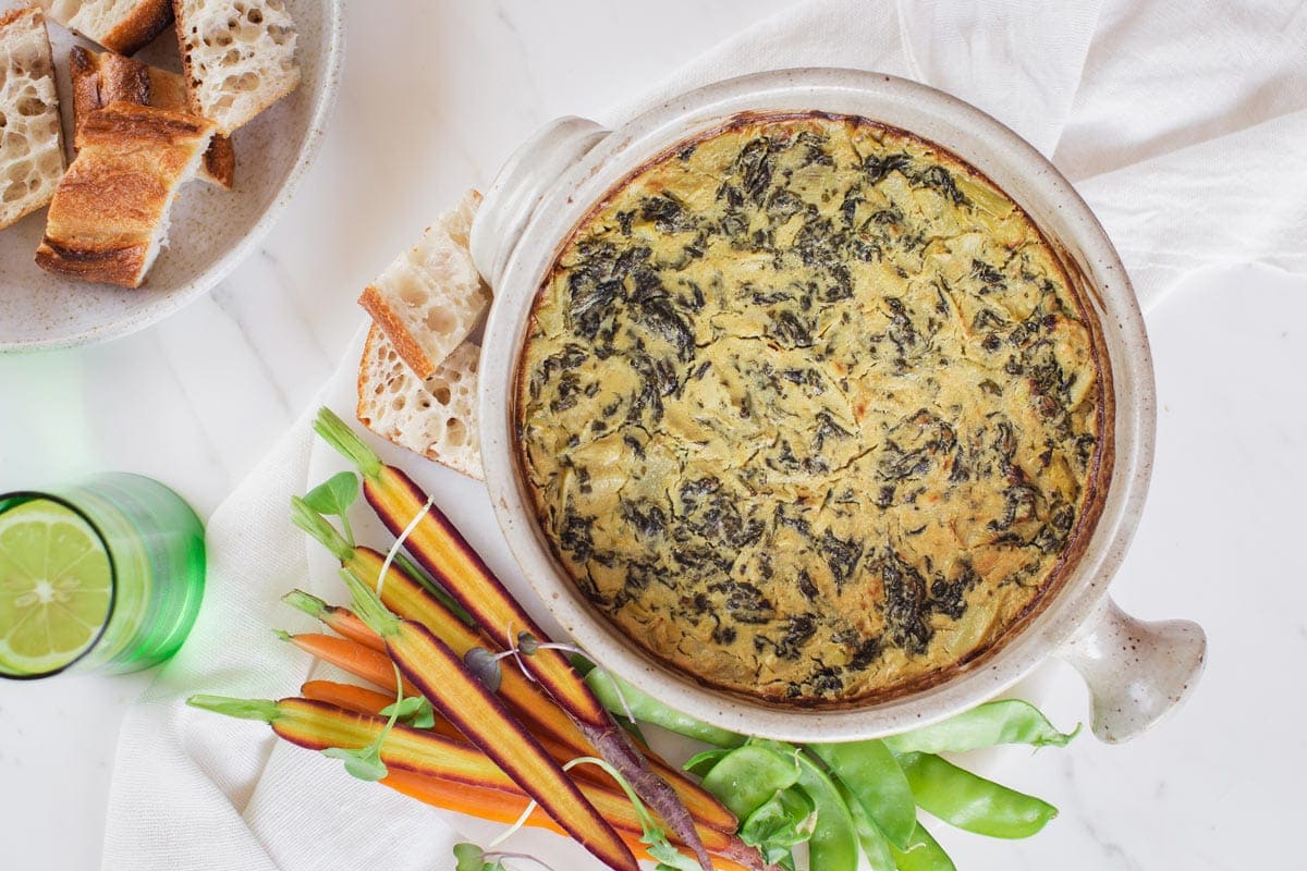 Freshly baked cheesy spinach dip ready to enjoy, with a side of bread and vegetable sticks