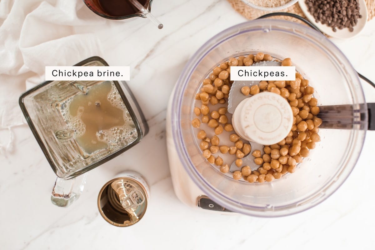 Blender containing chickpea liquid, and a food processor containing whole chickpeas, with a chickpea can beside it