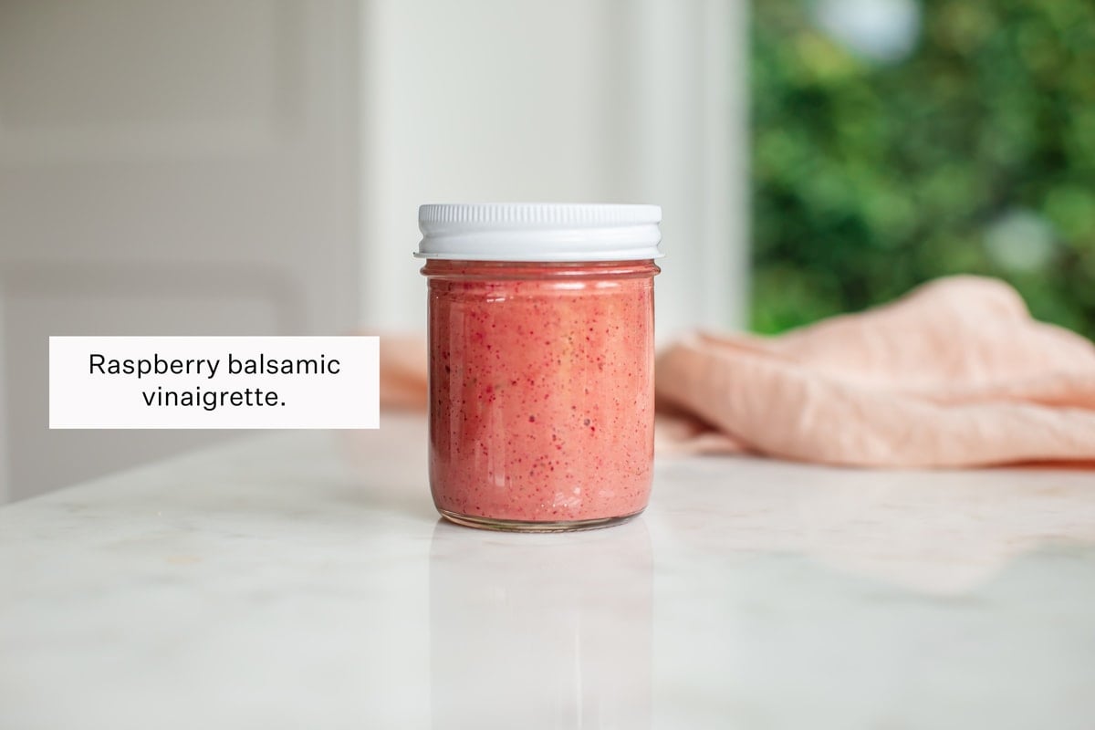 A jar of bright pink raspberry balsamic vinaigrette on the kitchen bench