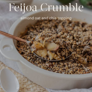 A baking dish filled with freshly baked feijoa crumble, with fruit and crumble heaped on a serving spoon to show the texture. The text "apple feijoa crumble" is written over the top, with the Ascension Kitchen logo at the bottom.