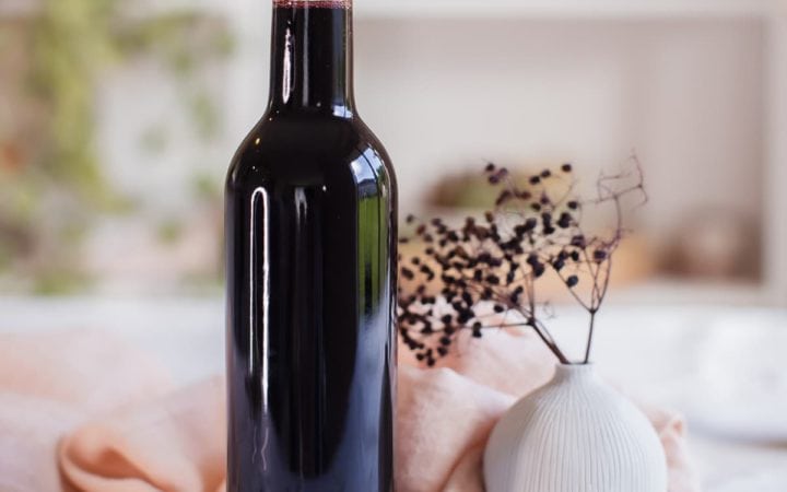 Bottle of rich purple coloured elderberry syrup capped with a cork