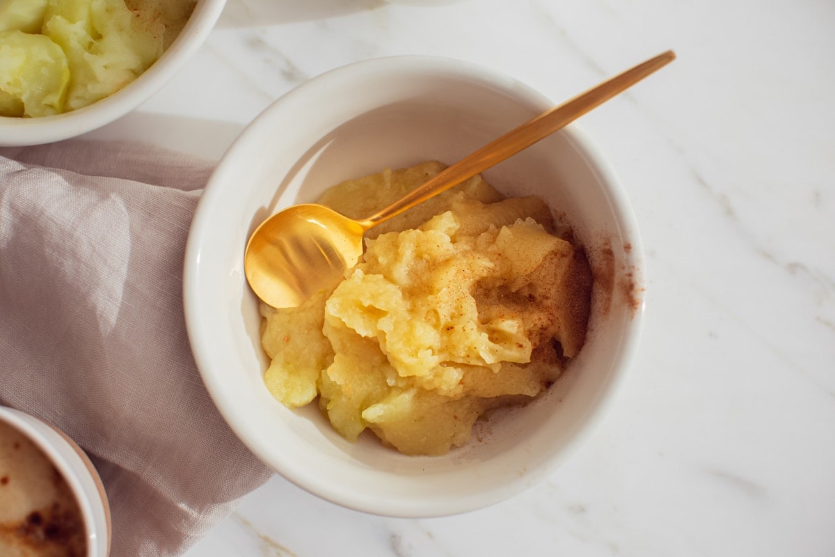Close up of a bowl of freshly made applesauce, with a little added slippery em for extra gut benefits. Golden spoon and dusting of cinnamon to finish.