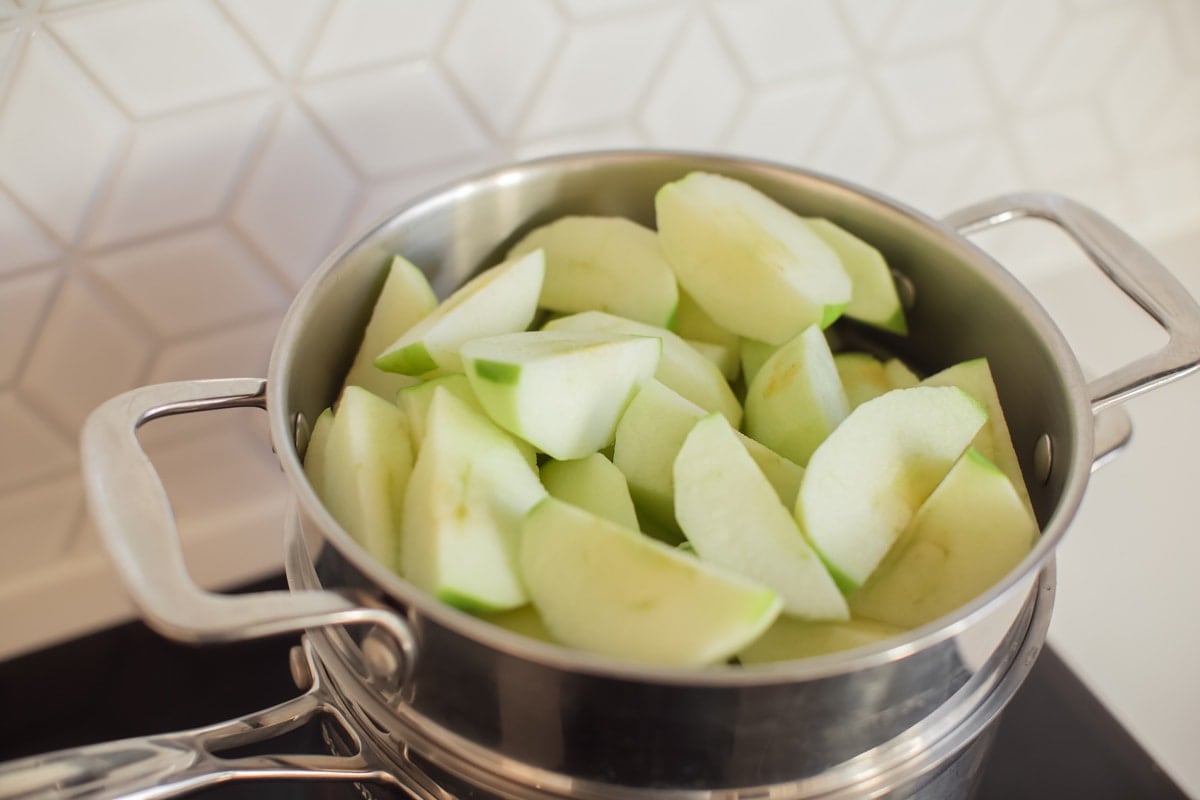 Overhead shot of a steamer over a saucepan, filled with chopped apples.