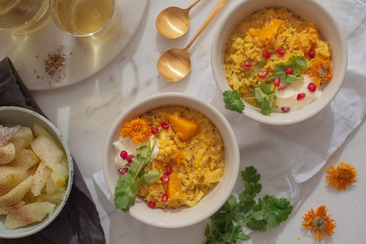 Two bowls of kitchari with colourful healthy toppings - cilantro, dried calendula flowers, coconut yoghurt and pomegranate arils.