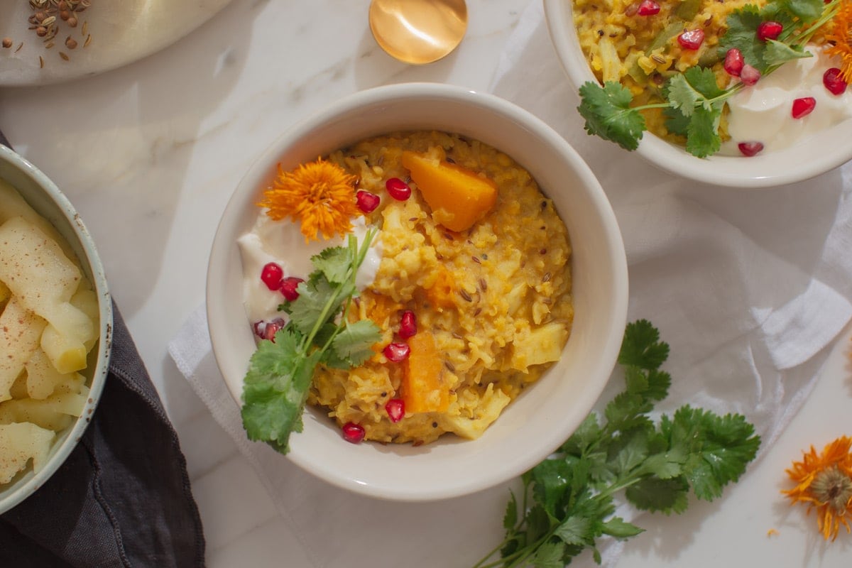 Close up of a bowl of kitchari, on a marble surface, toppings scattered around the background.