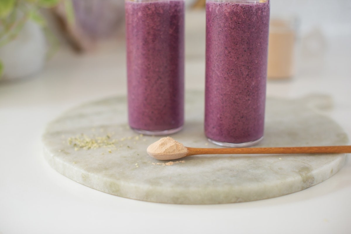 Close up of a wooden spoon heaped with dried lucuma powder, on a marble kitchen surface.