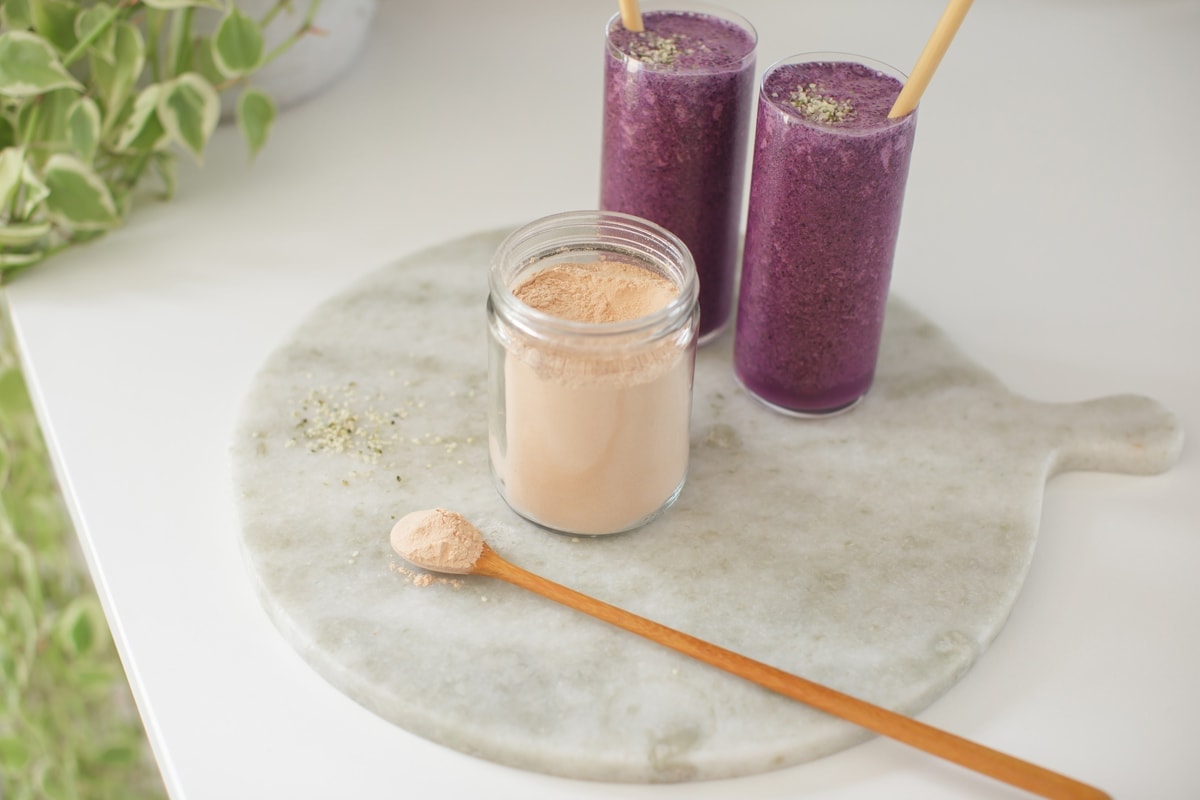 Jar of lucuma powder on a marble platter with a wooden spoon beside it.