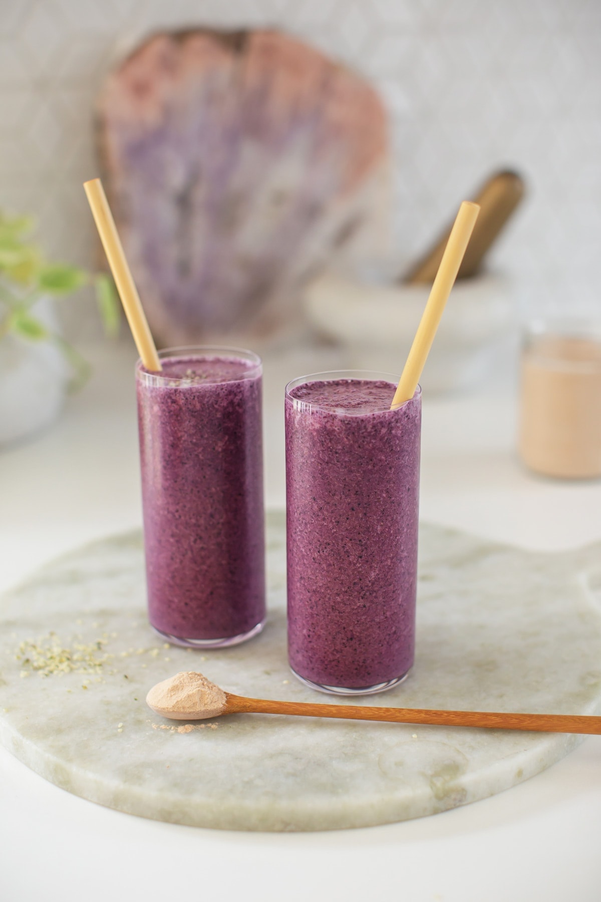 Two beautiful purple smoothies made with lucuma, each with wooden straws, on the kitchen bench top.