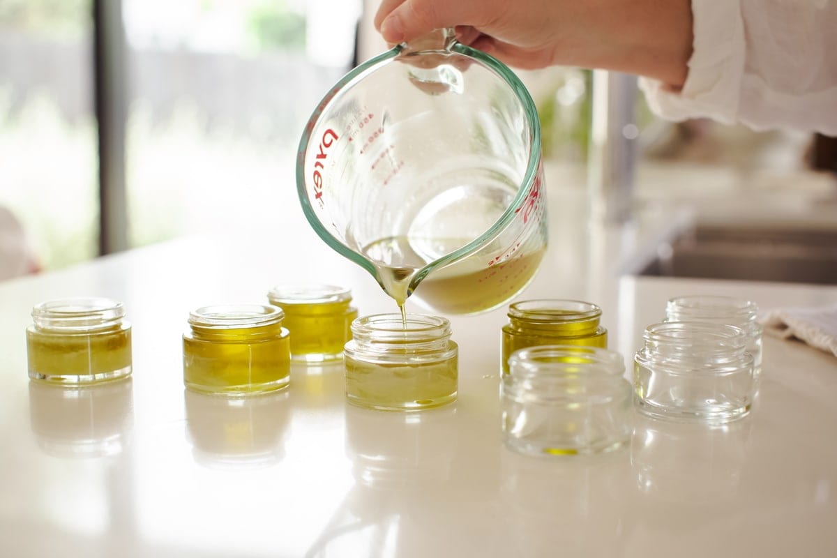 Lauren pouring the liquid salve into multiple small glass jars.