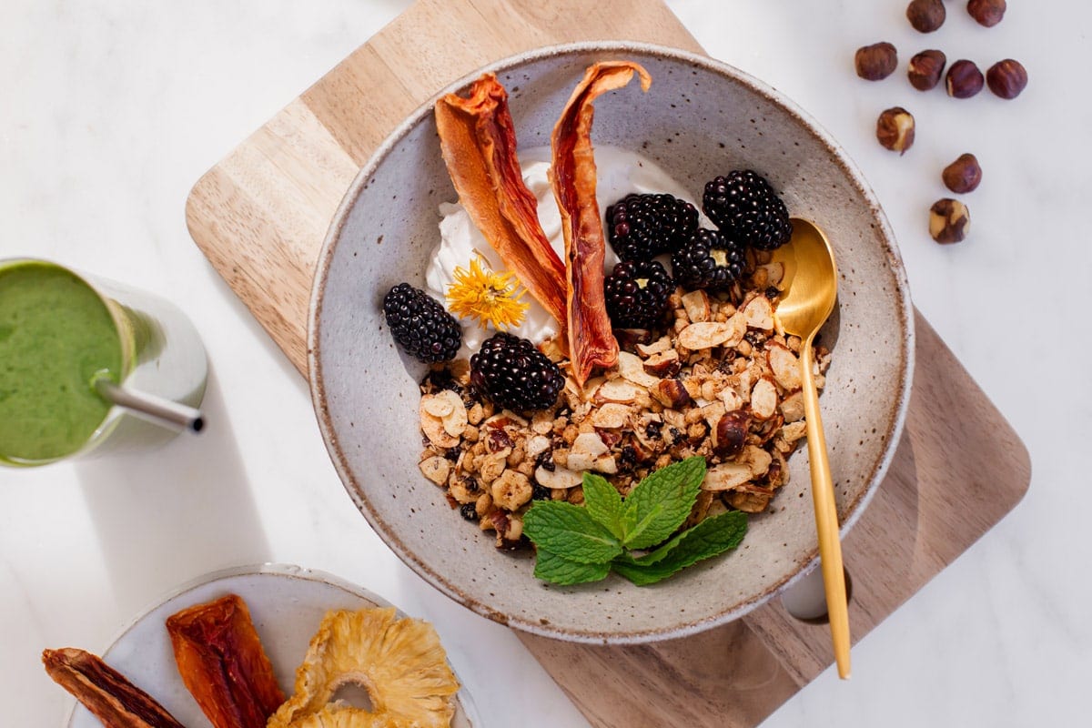 A ceramic bowl filled with crunchy granola, coconut yoghurt, blackberries and papaya.