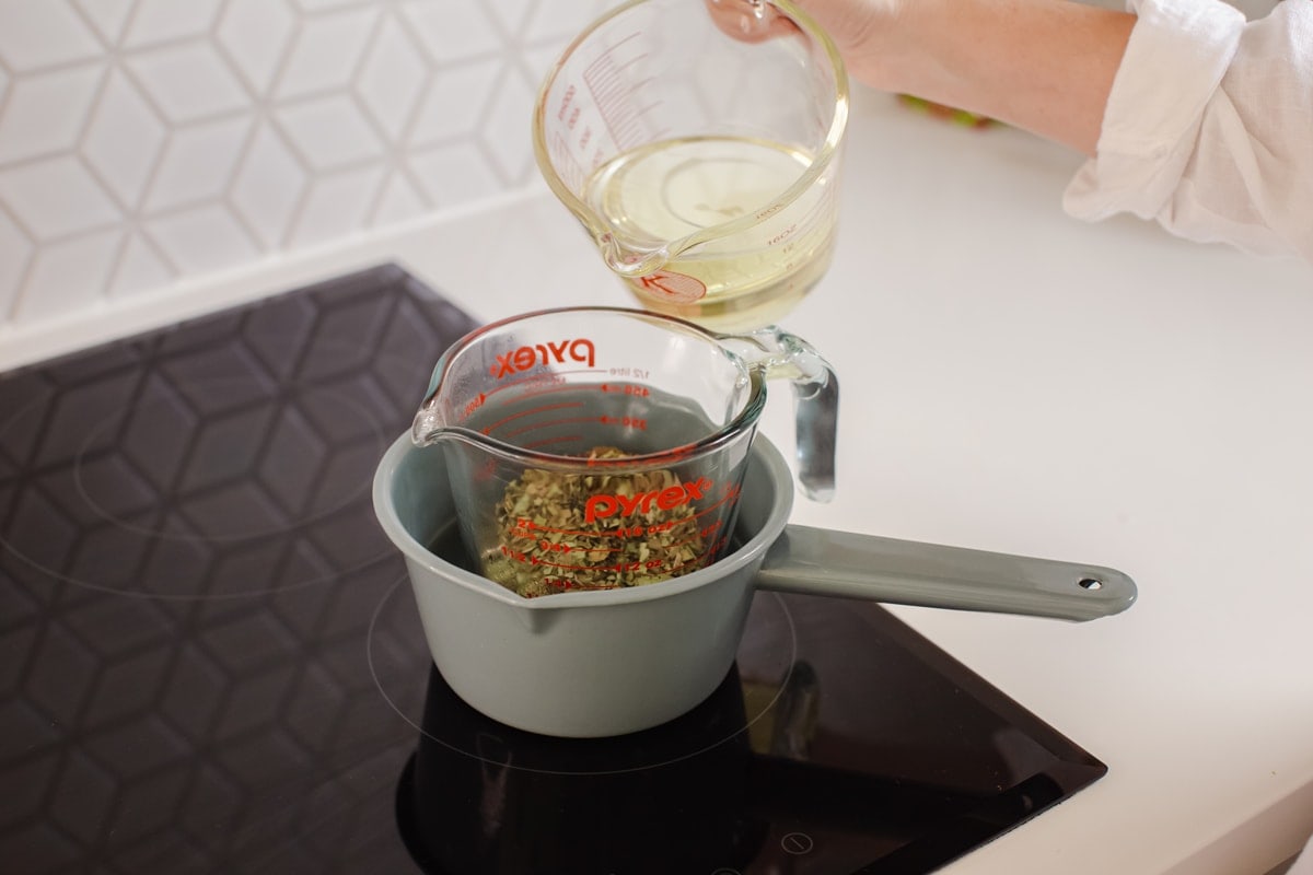 Lauren pouring sweet almond oil over dried plantain herb, in a double boiler.