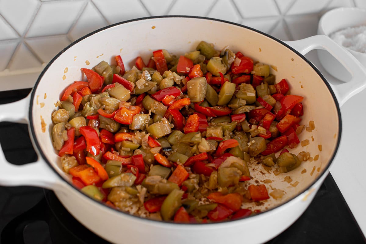 Well cooked eggplant and bell peppers with a few other ingredients in a heavy-bottomed saucepan on the stove