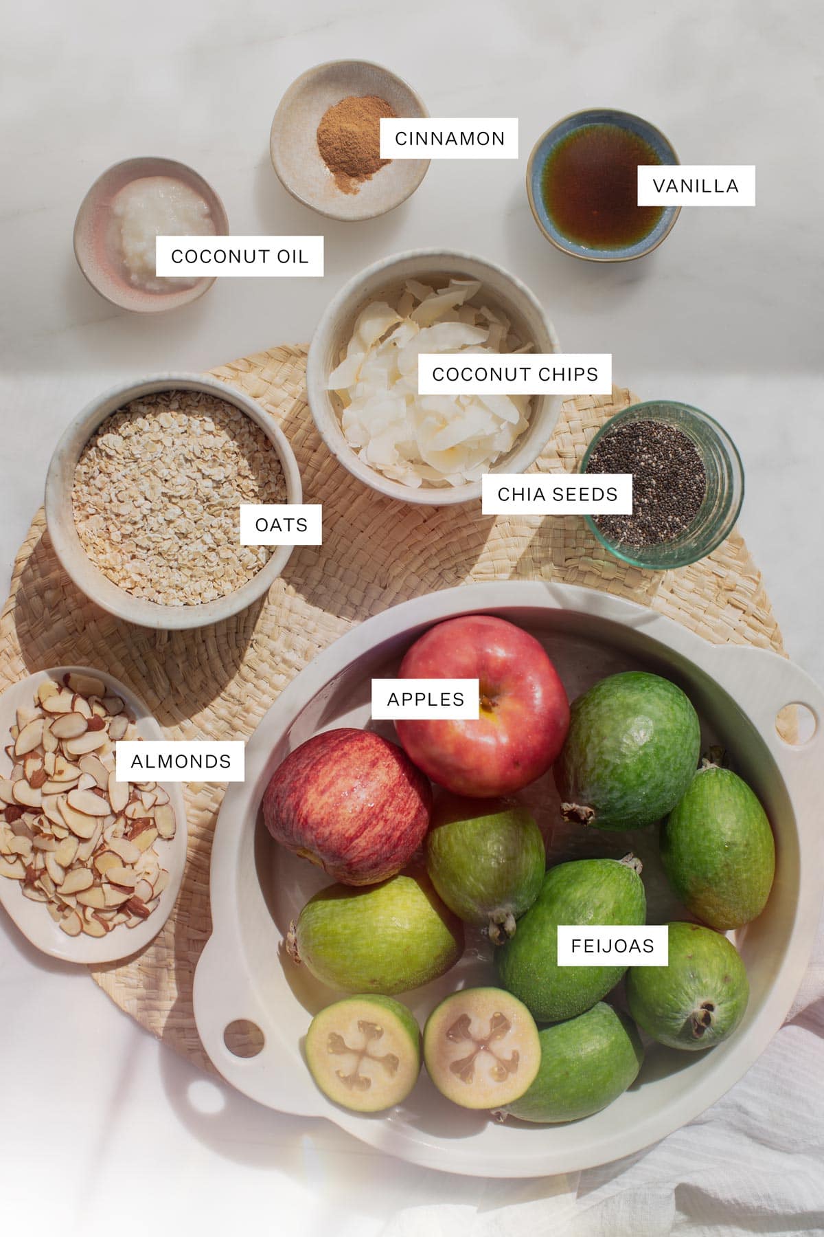 Flat lay of all the ingredients needed for this recipe - including feijoas, apples, oats, almonds, coconut flakes, cinnamon, chia, coconut oil, maple syrup