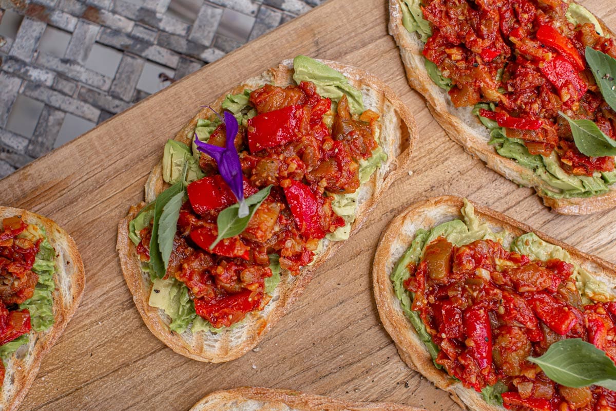 Close up of a several slices of toasted sourdough topped with smashed avocado and homemade matbucha, ready to serve to guests.