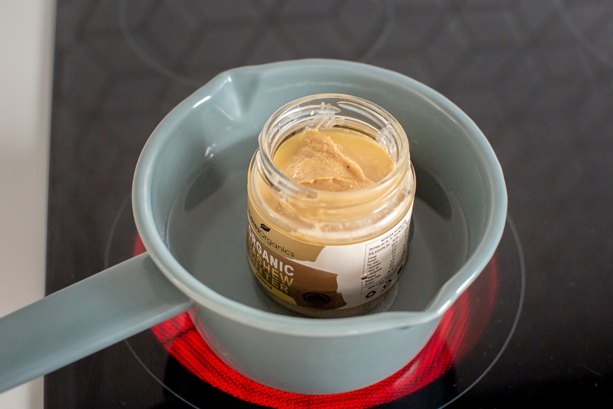A jar of cashew butter resting in a saucepan filled with simmering water to help soften it, for ease of blending
