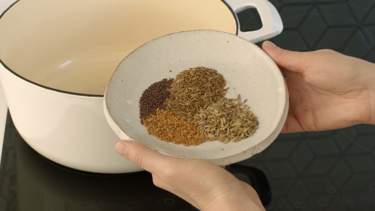 A dish filled with whole spices - mustard, fenugreek, fennel and cumin, about to go into the pot