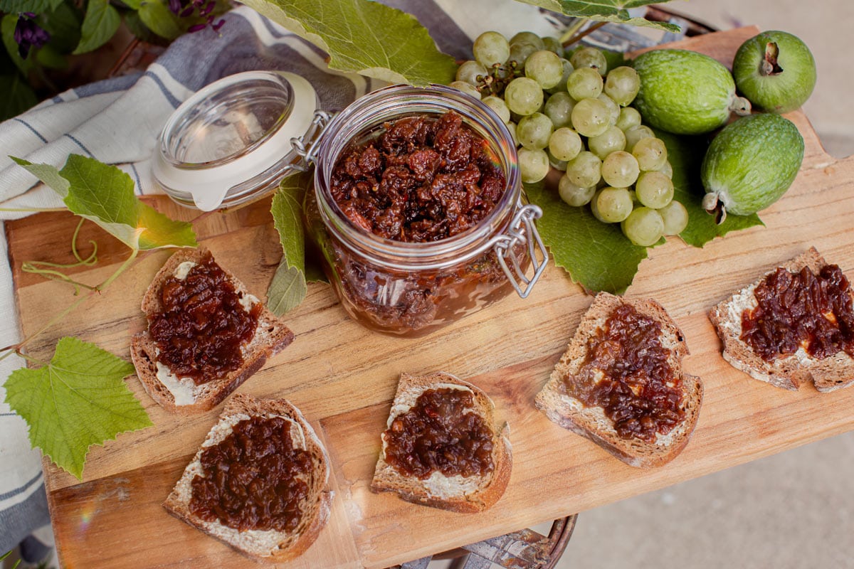 A serving platter on a rustic chair in the garden, filled with slices of rye sourdough topped with chutney, organic grapes and feijoa fruits