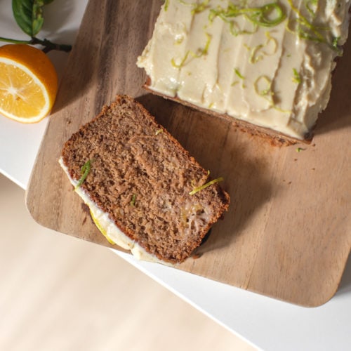 A slice of feijoa loaf iced with a lemon cashew cream, on a wooden board