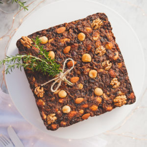 A whole gluten free fruit cake on a cake stand, with fairy lights in the background.