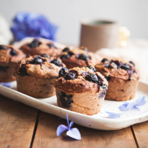 A speckled platter filled with freshly baked teff muffins, a cup of tea in the background.