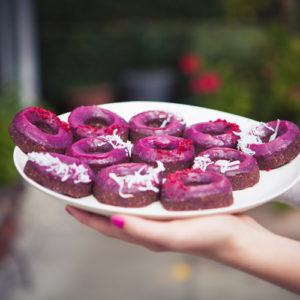 Lauren holding a plate filled with healthy doughnuts glazed with pink icing, made from raw food ingredients.