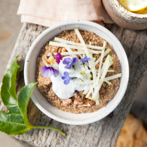 Bowl of quinoa porridge on a rustic bench outdoors, with a mug of hot tea nearby.