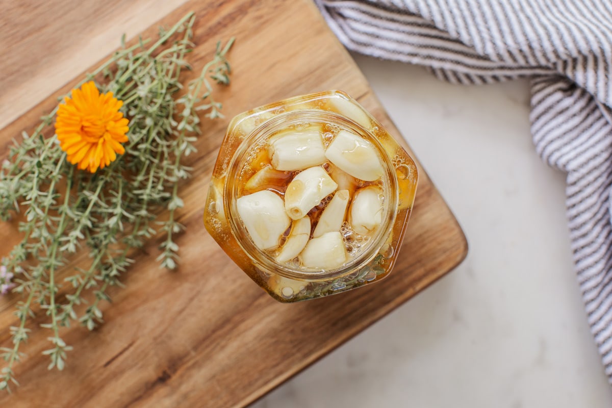 Birds eye view of an open jar filled to the brim with garlic cloves, covered with honey. The garlic cloves have bobbed to the surface.