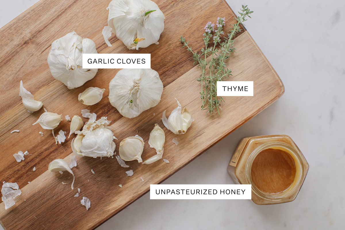 Ingredients used to make fermented garlic honey on a wooden board: garlic, thyme and unpasteurized honey.