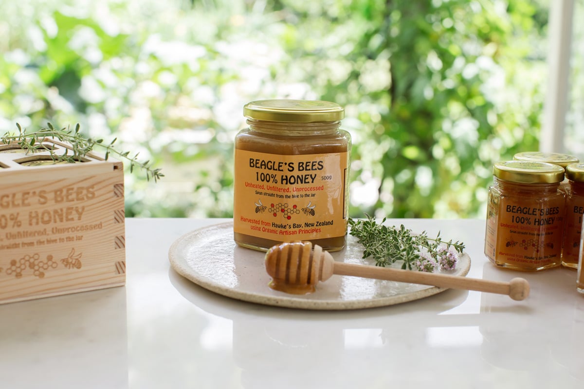 Large jar of raw, organic, ethical honey on a ceramic plate, with a honey dipper and fresh thyme.