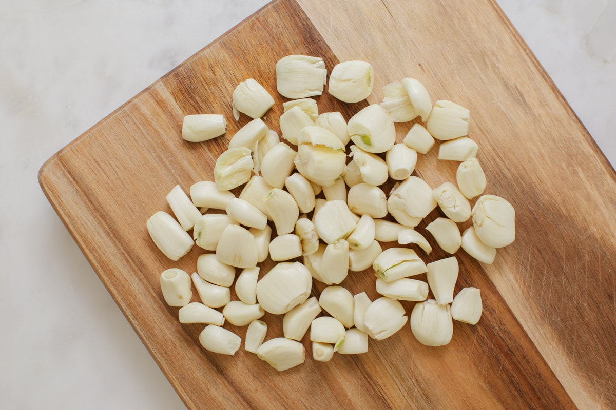 Wooden board with about a cups' worth of freshly peeled garlic cloves that have been lightly bruised with a knife.