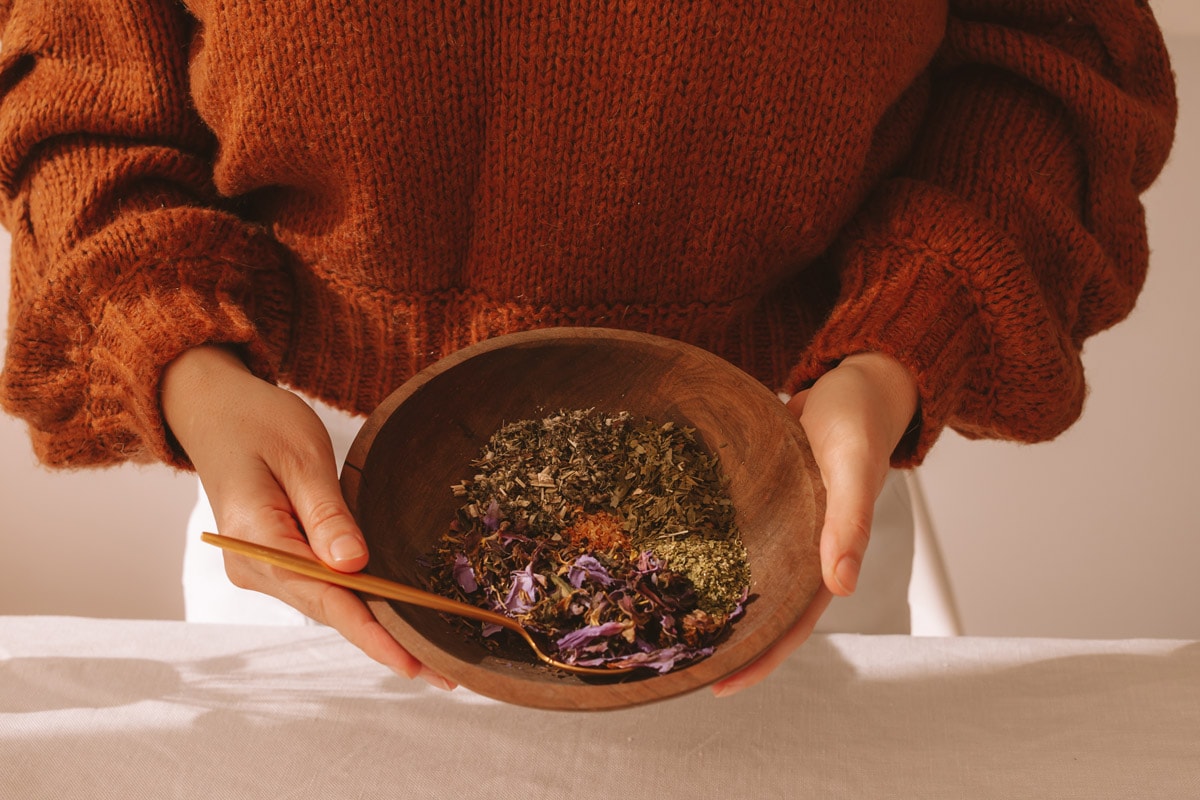 Lauren holding a wooden bowl filled with the herbs needed to make a lucid dreaming tea blend: mugwort, blue lotus flower, passionflower, ginkgo and orange peel.