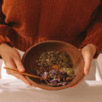 Woman holding a wooden bowl filled with a mixture of herbs to aid lucid dreams.
