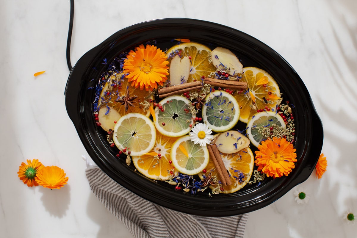A crockpot filled with water, sliced citrus, aromatic spices and bright calendula flowers. The lid is off to allow the scent to travel.