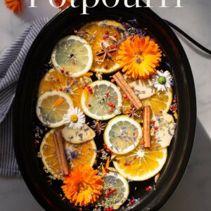 A crockpot, filled with water, citrus, fowers and aromatic spices. Text over the top reads "Crockpot Potpourri".
