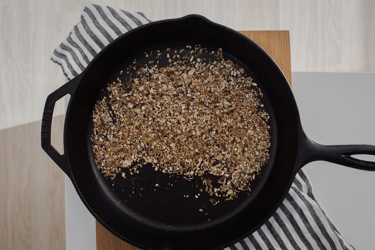 Overhead shot of a cast iron pan on a kitchen bench, with freshly toasted dandelion root.